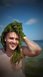 Portrait of smiling shirtless man with seaweed on head at beach 