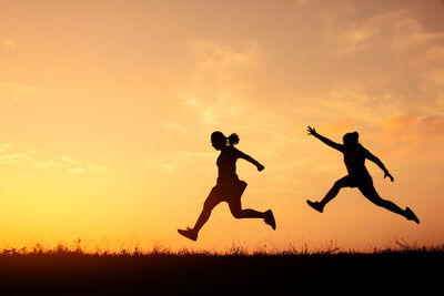 Silhouette people jumping on field against sky during sunset