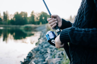 Man holding camera while standing by lake