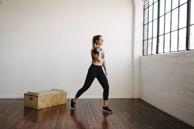 Female athlete carrying kettlebell while standing in gym