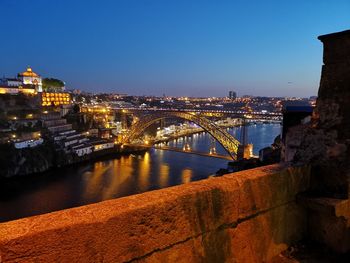 Illuminated bridge over river against buildings in city at night