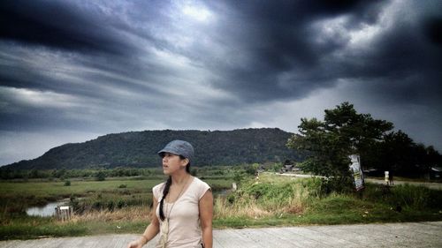 Person standing on grassy field against cloudy sky