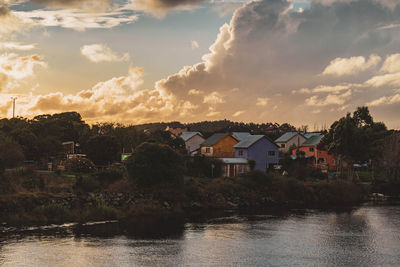 Houses by river against sky during sunset