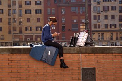 Man sitting on wall against buildings in city