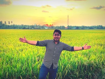 Woman with arms raised on field against sky during sunset