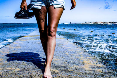 Low section of woman walking on pier amidst sea