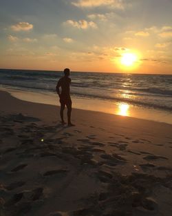 Full length of man standing on shore at beach during sunset