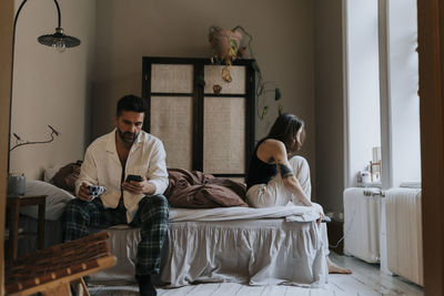 Man using smart phone with non-binary person wearing socks sitting on bed at home