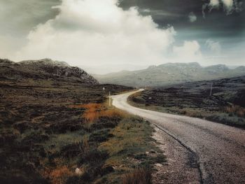 Country road leading towards mountains against sky