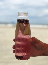 Close-up of hand holding drink at beach against sky