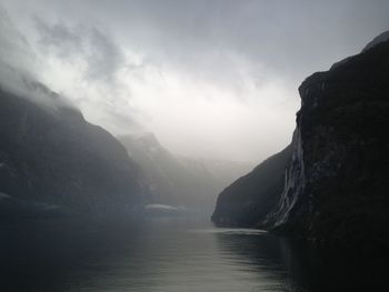 Scenic view of river amidst mountains against sky during foggy weather