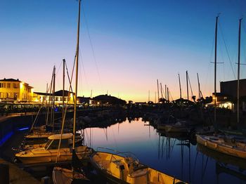 Sailboats moored in harbor at sunset