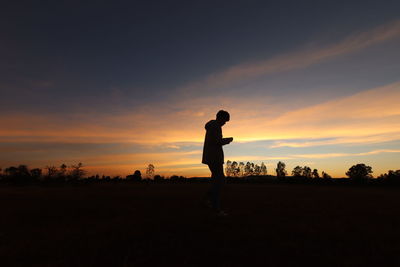 Silhouette man standing on field against sky during sunset