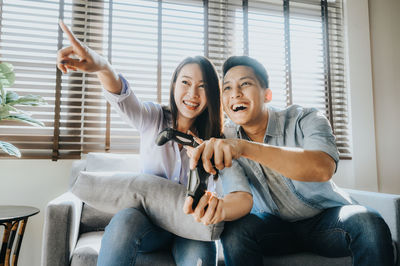 Smiling couple playing video game while sitting on sofa at home