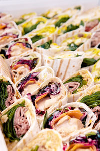 Abundance of tasty tortilla rolls with different fillings served on table with colorful tablecloth near wall during festive event