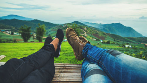 Low section of people relaxing on land against sky