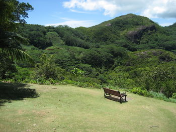 Empty bench on green landscape against sky