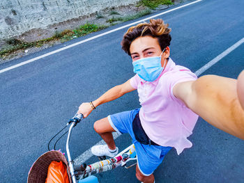 Portrait of smiling teenager boy wearing mask riding bicycle on road