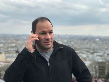 Man talking on phone while standing against cityscape