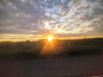 Sunlight streaming on field against sky during sunset