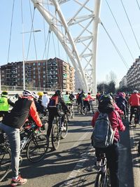 Rear view of people riding bicycle on bridge in city