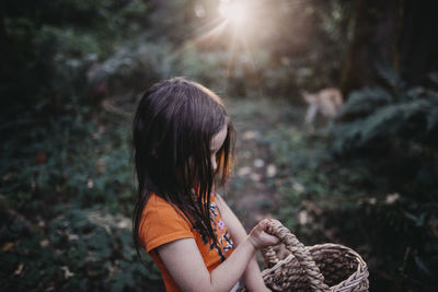 Side view of girl with wicker basket standing at forest
