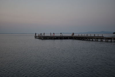 People on pier at sea against sky during sunset