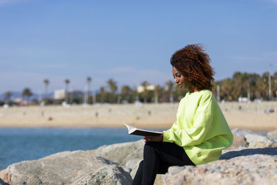 Woman reading book while sitting on rock