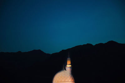 Silhouette of mountain range with illuminated mosque against blue sky