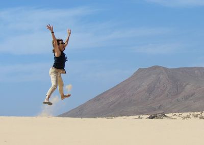 Full length of woman jumping in desert against sky
