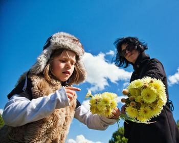 Low angle view of mother and daughter holding dandelions against sky