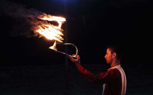 Side view of man holding lit fire at night