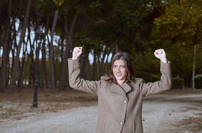 Portrait of smiling woman with arms raised standing on road