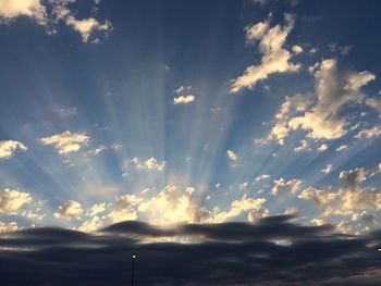 Low angle view of sunlight streaming through clouds