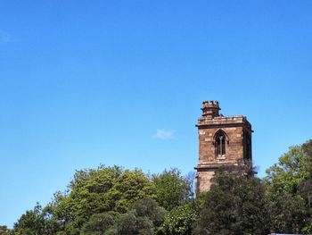 Low angle view of trees and building against blue sky