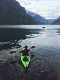 Rear view of man in boat on lake against mountains and sky