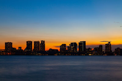 Sea by buildings against sky during sunset