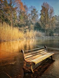 Empty bench by lake against sky