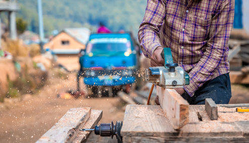 Midsection of carpenter cutting wooden material at work shop