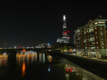 Illuminated buildings by river against sky at night