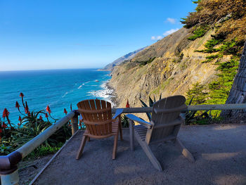 Chairs and table on beach against blue sky