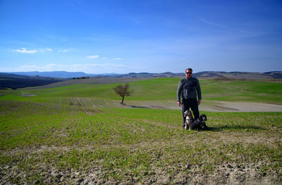 Mature man with dogs standing on grassy field against blue sky