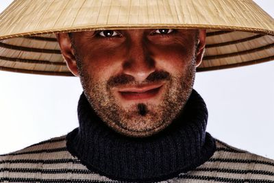 Portrait of mid adult man wearing asian style conical hat against white background