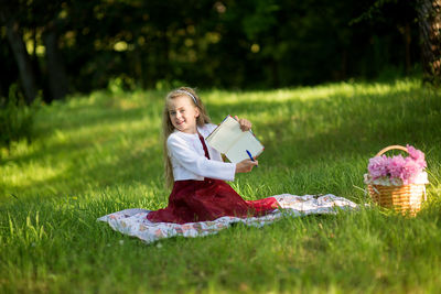 Portrait of girl holding book and pen while sitting on grass