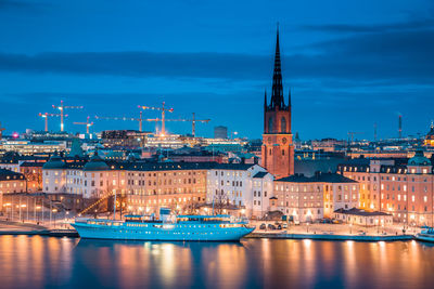 Sailboats in river by illuminated buildings against sky in city