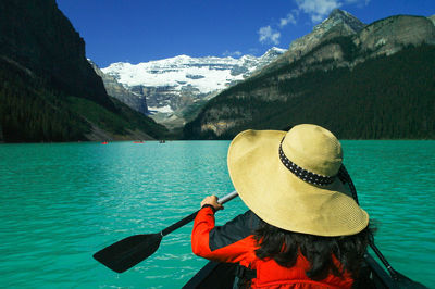Rear view of woman wearing hat canoeing on lake