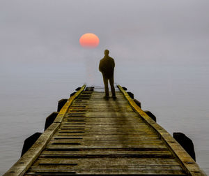 Rear view of man standing on pier over sea against sky