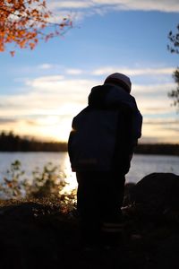 Rear view of man looking at lake against sky