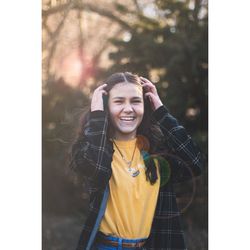 Portrait of cheerful young woman standing against tree
