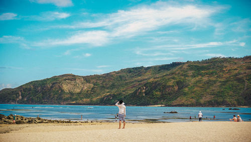 Rear view of people standing on beach against sky